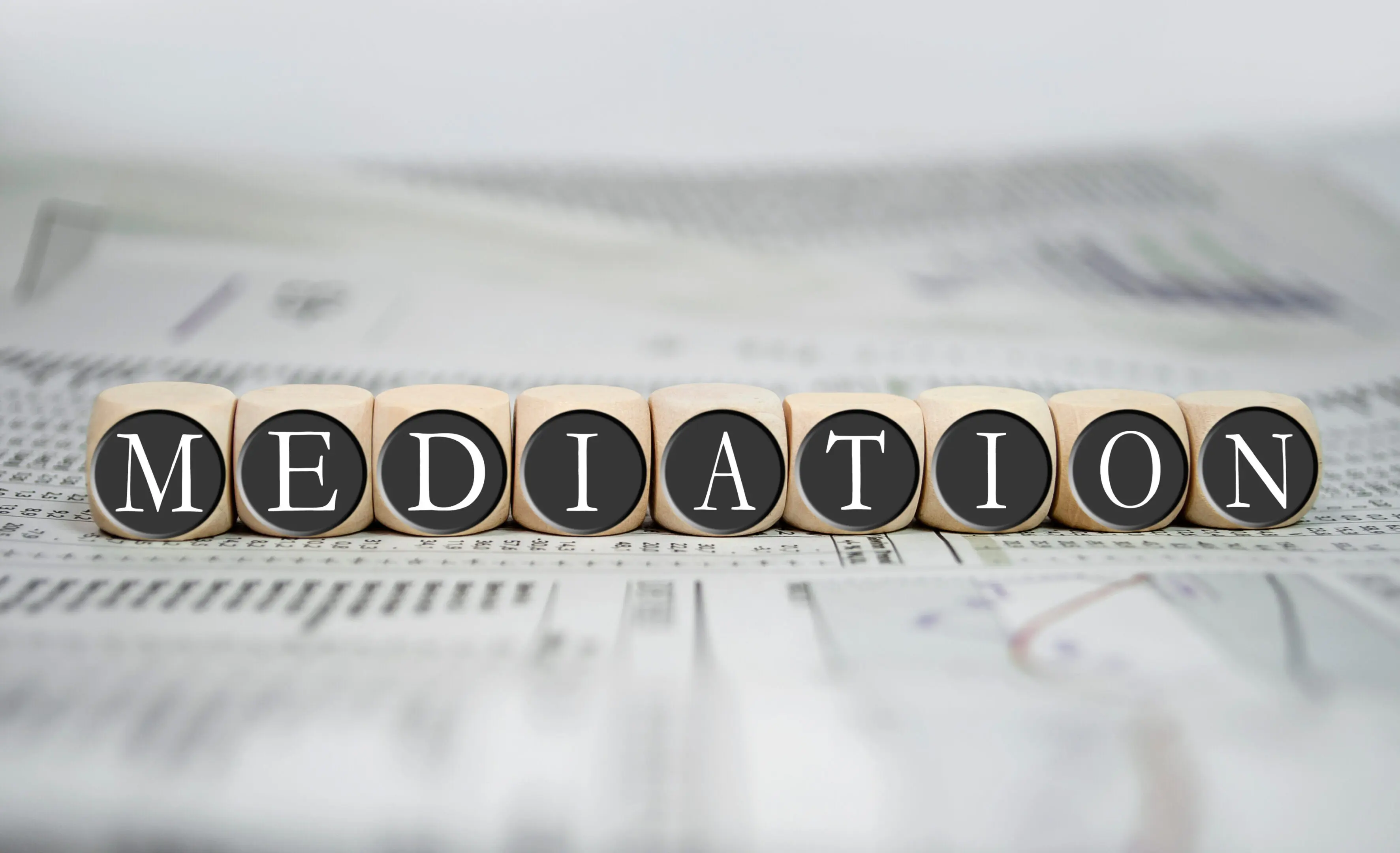 Wooden blocks spelling 'MEDIATION' on a newspaper background.