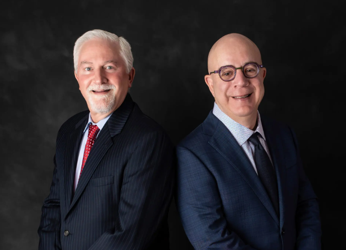 Two elderly men in suits smiling against a black background.