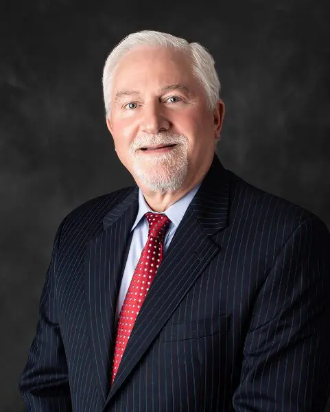 Elderly man in a suit smiling against a dark background.